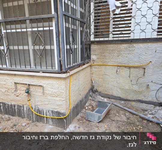 צינור גז צהוב מחובר לקיר חיצוני ליד חלון עם סורגים